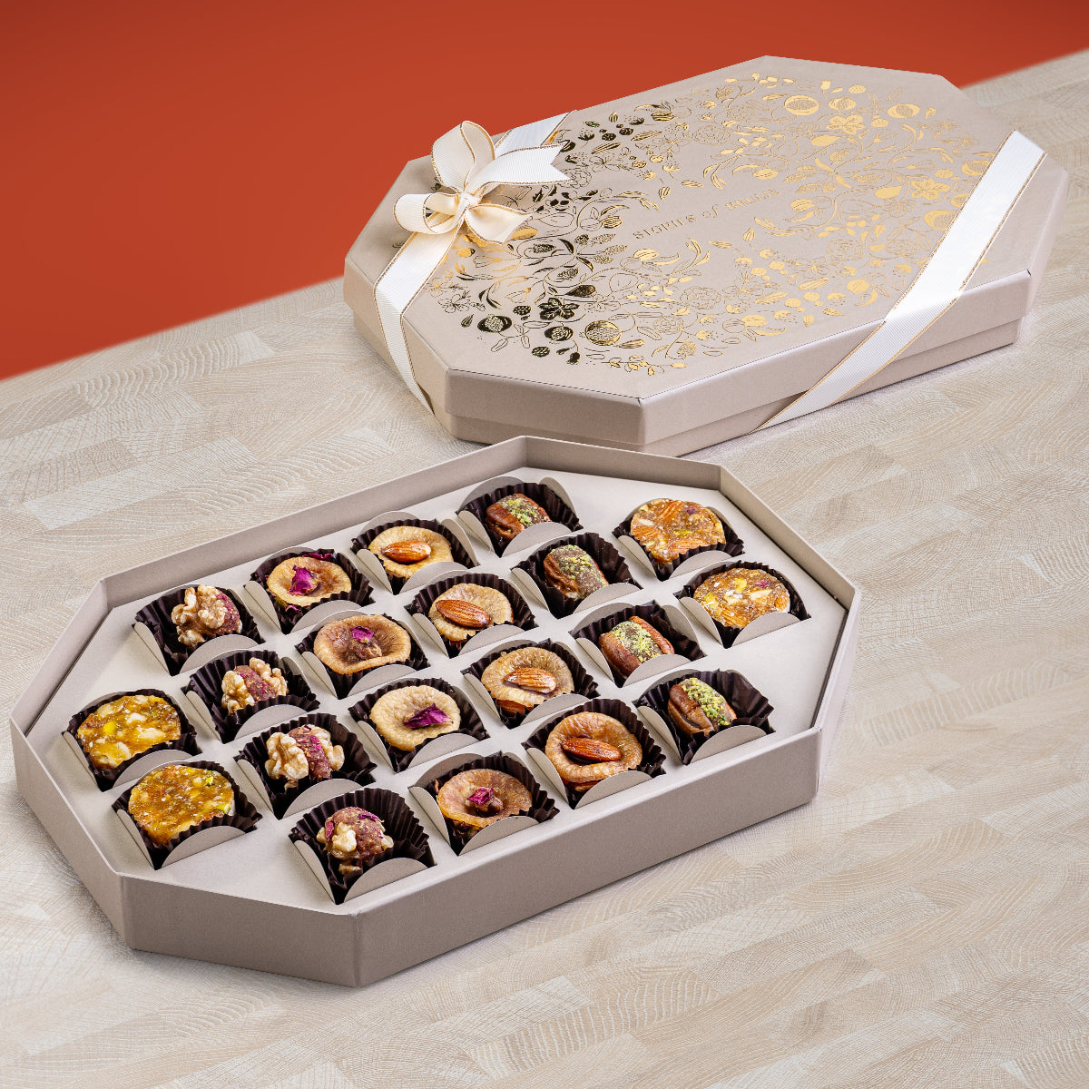 Elegant cream Ruby Box with gold floral design and ribbon, holding an assortment of fig & nut bites, saffron pistachio rose figs, stuffed dates, and apricot nut bites.