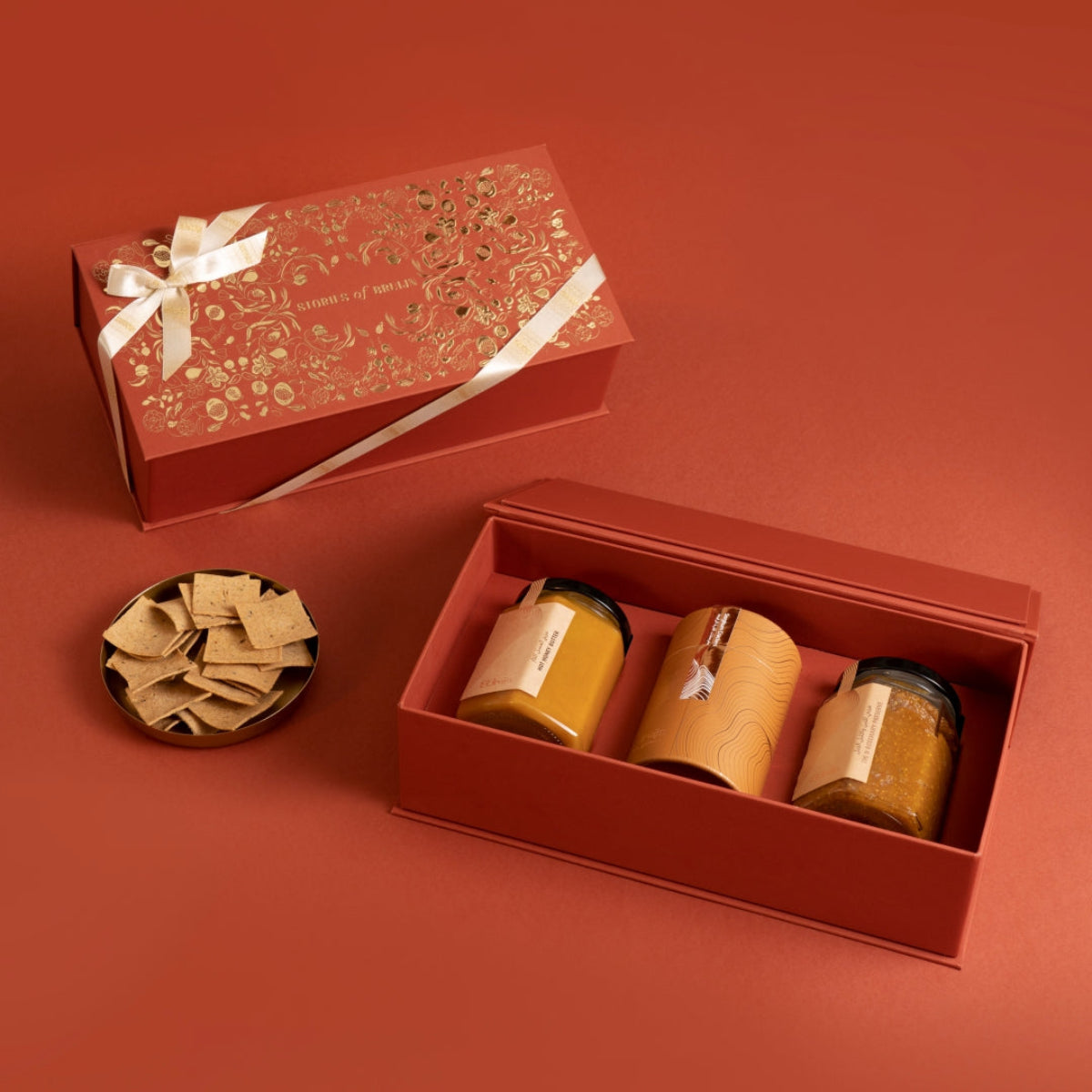 Open red festive gift box with Hot Honey Butter, Fig & Rosemary Spread, and sorghum chips in jars, ideal for gourmet gifting.