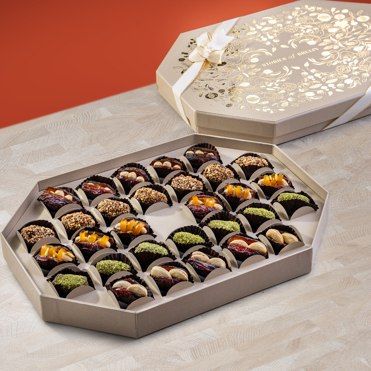 Elegant cream Ruby Box with gold floral design and ribbon, featuring an assortment of stuffed Mejdool dates filled with macadamias, cashews, pistachios, and tamriyas.