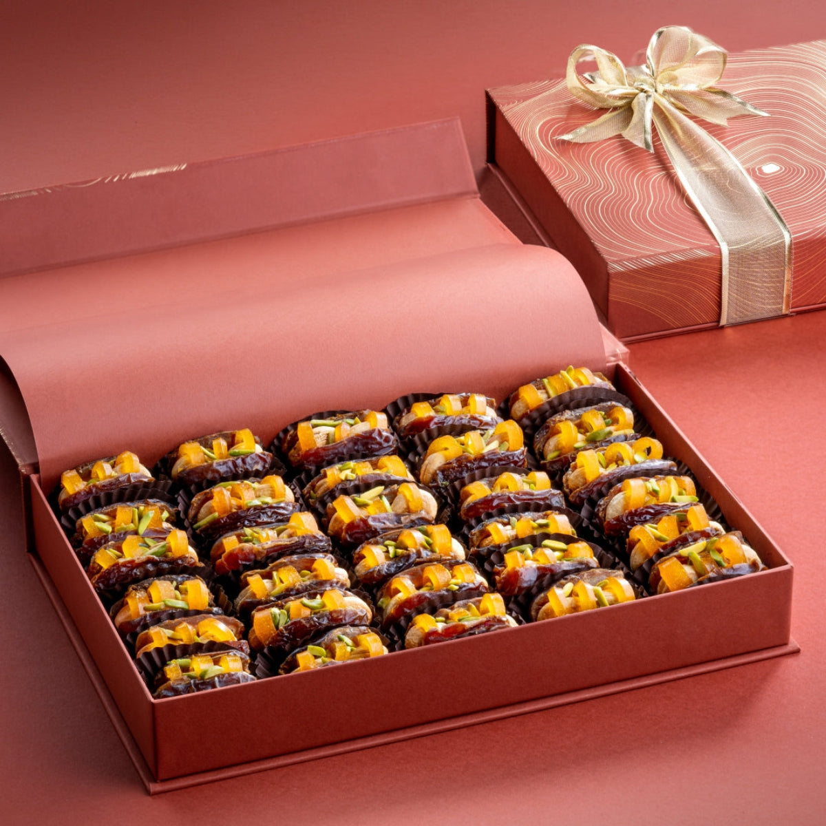 Open rust gift box filled with mejdool dates stuffed with dried mango and roasted cashew, presented as a healthy vegan treat.