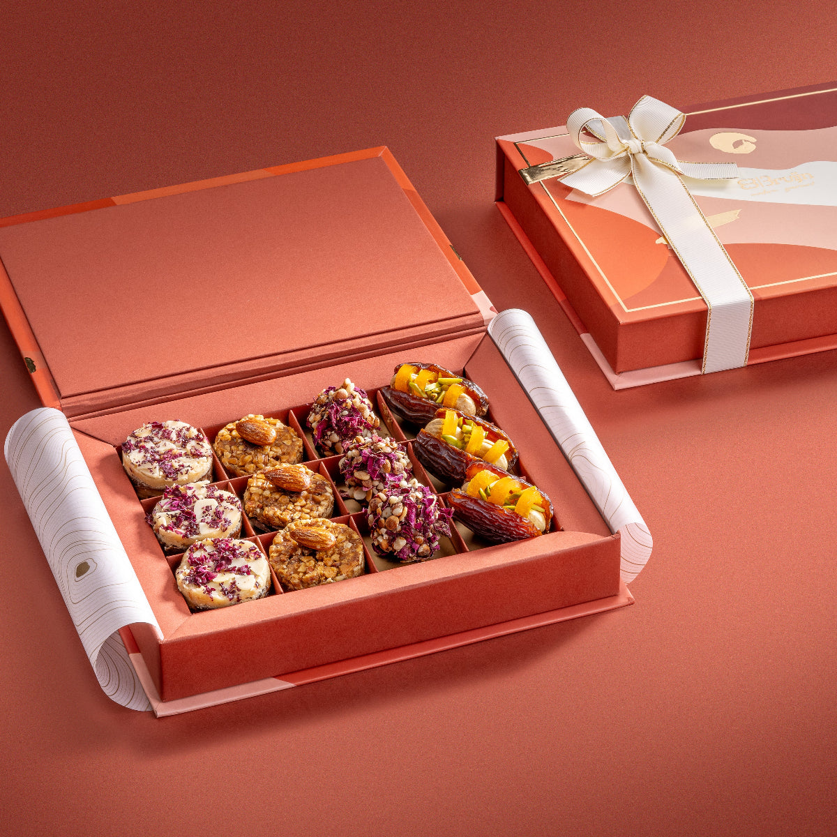 Open Assorted Delights Box with patterned lid and ribbon, showcasing neatly arranged Persian rose delights, fig bites, date truffles, and stuffed dates.