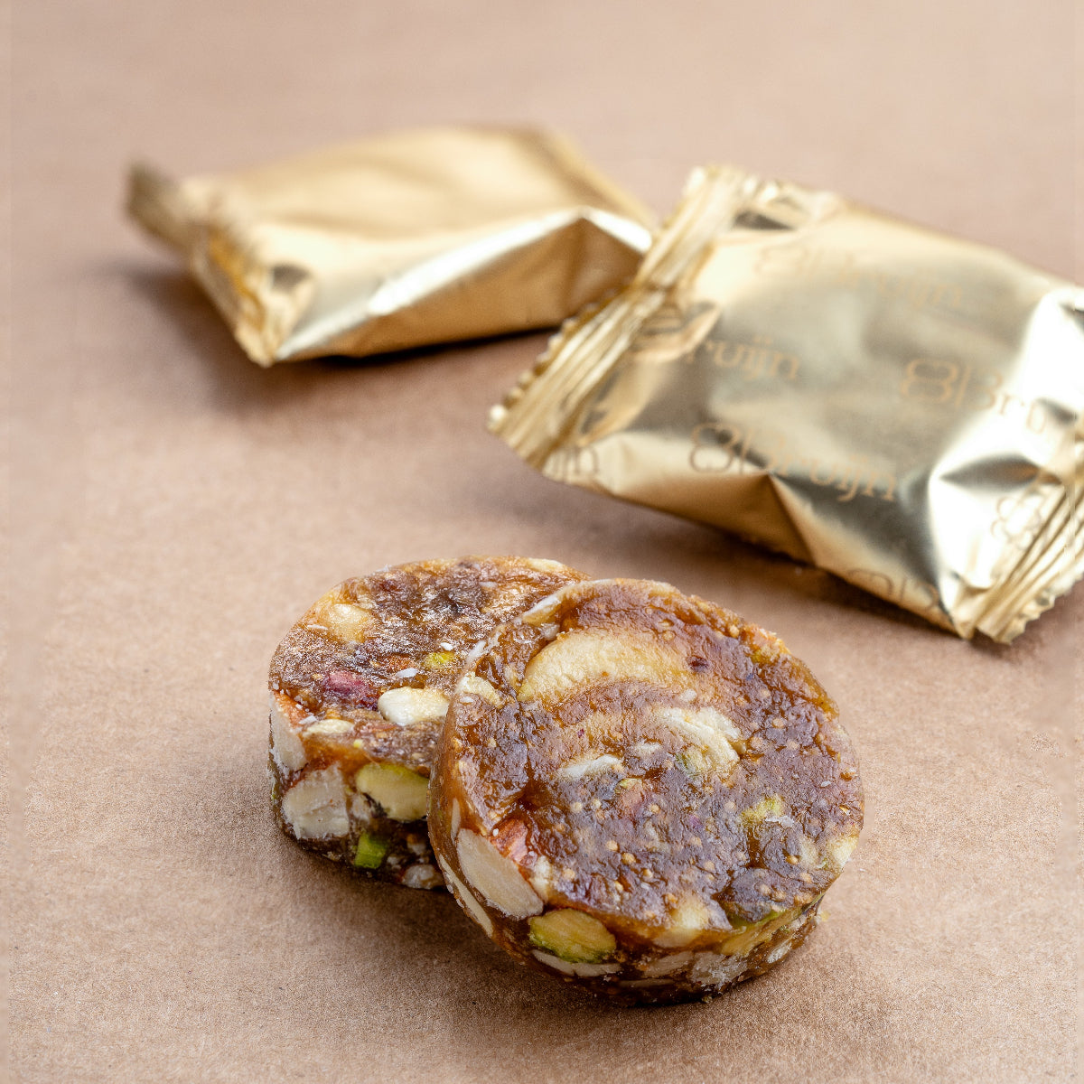 Close-up of fig & nut bites with roasted nuts rolled in grainy fig paste, individually wrapped in gold foil.
