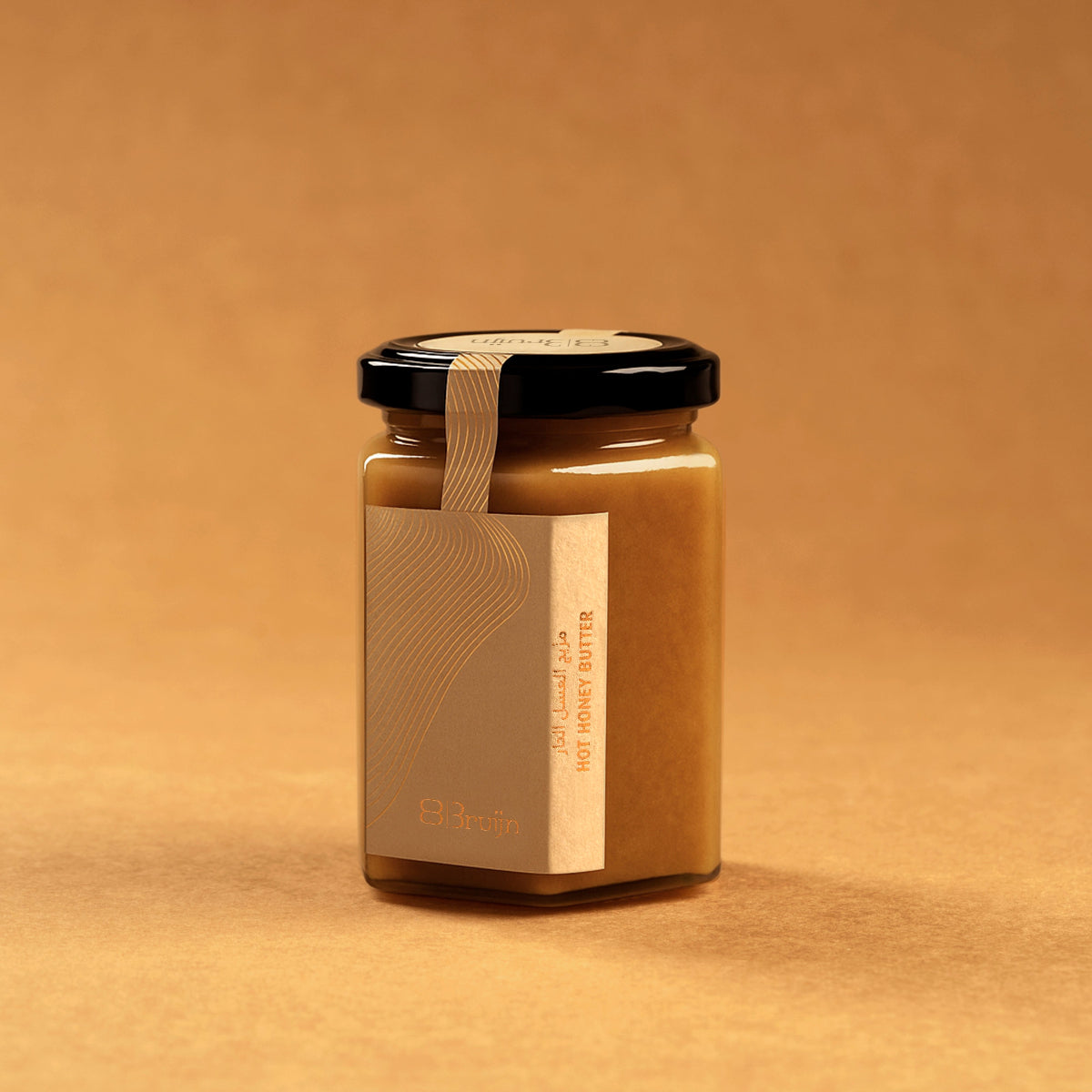 Glass jar of Bruijn Hot Honey Butter with black lid and kraft label, filled with a golden-red blend of garlic, red chillis, and raw honey.