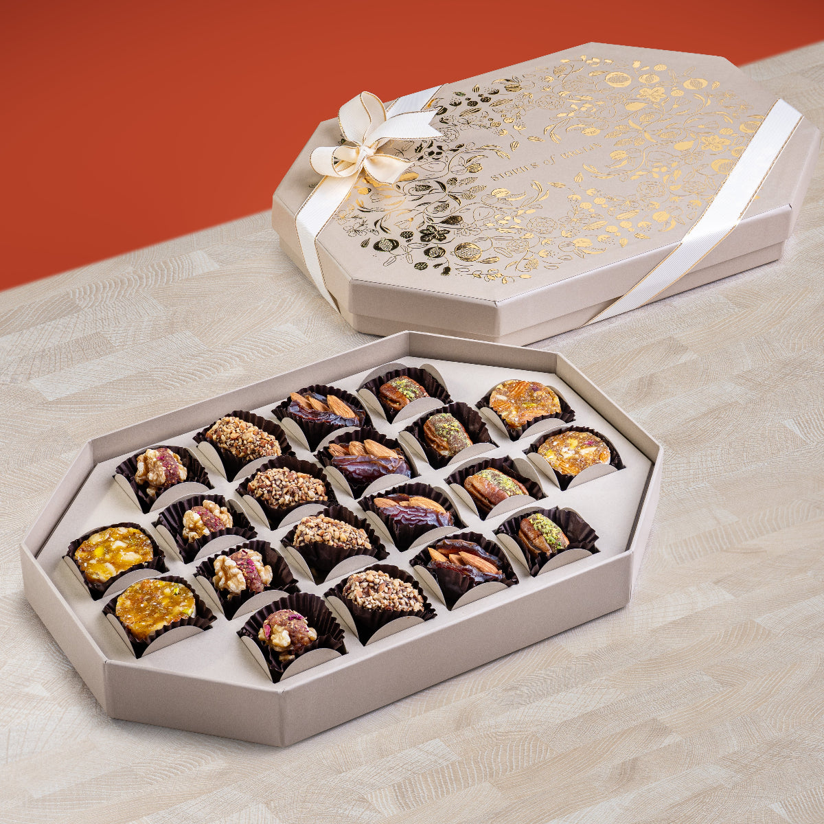Elegant cream Ruby Box with gold floral design and ribbon, containing an assortment of fig bites, stuffed dates, and nut-filled dried fruits arranged in a festive tray.