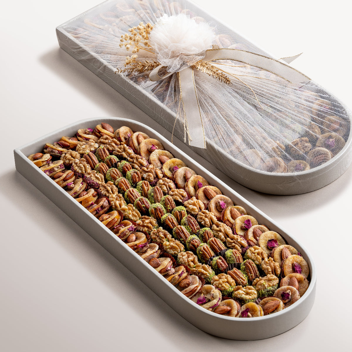 Large oval tray with assorted figs stuffed with nuts, saffron pistachio, rose, and pecan-date wholes.Elegant oval tray wrapped with sheer fabric and floral detail, perfect for gifting.