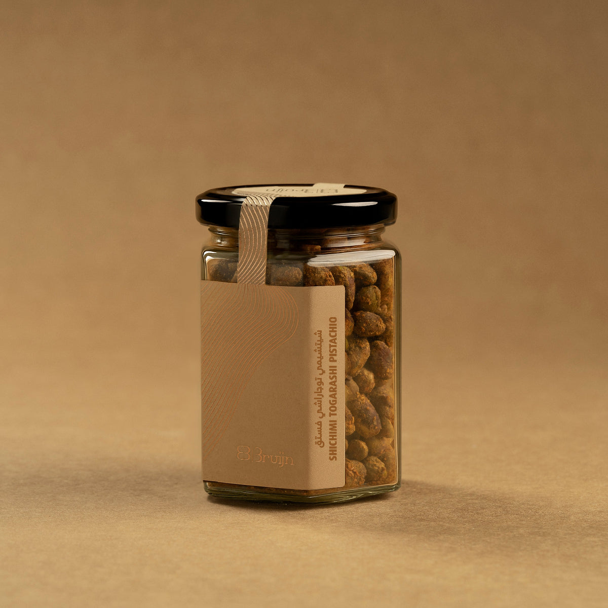 Glass jar of Bruijn Shichimi Togarashi Pistachios with black lid and kraft label, filled with pistachios coated in a spicy Japanese seasoning blend.