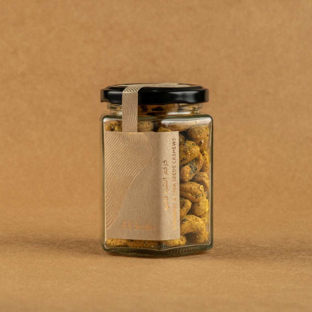 Glass jar of Bruijn Turmeric & Chia Seed Cashews with black lid and kraft label, filled with golden turmeric-coated cashews speckled with chia seeds.