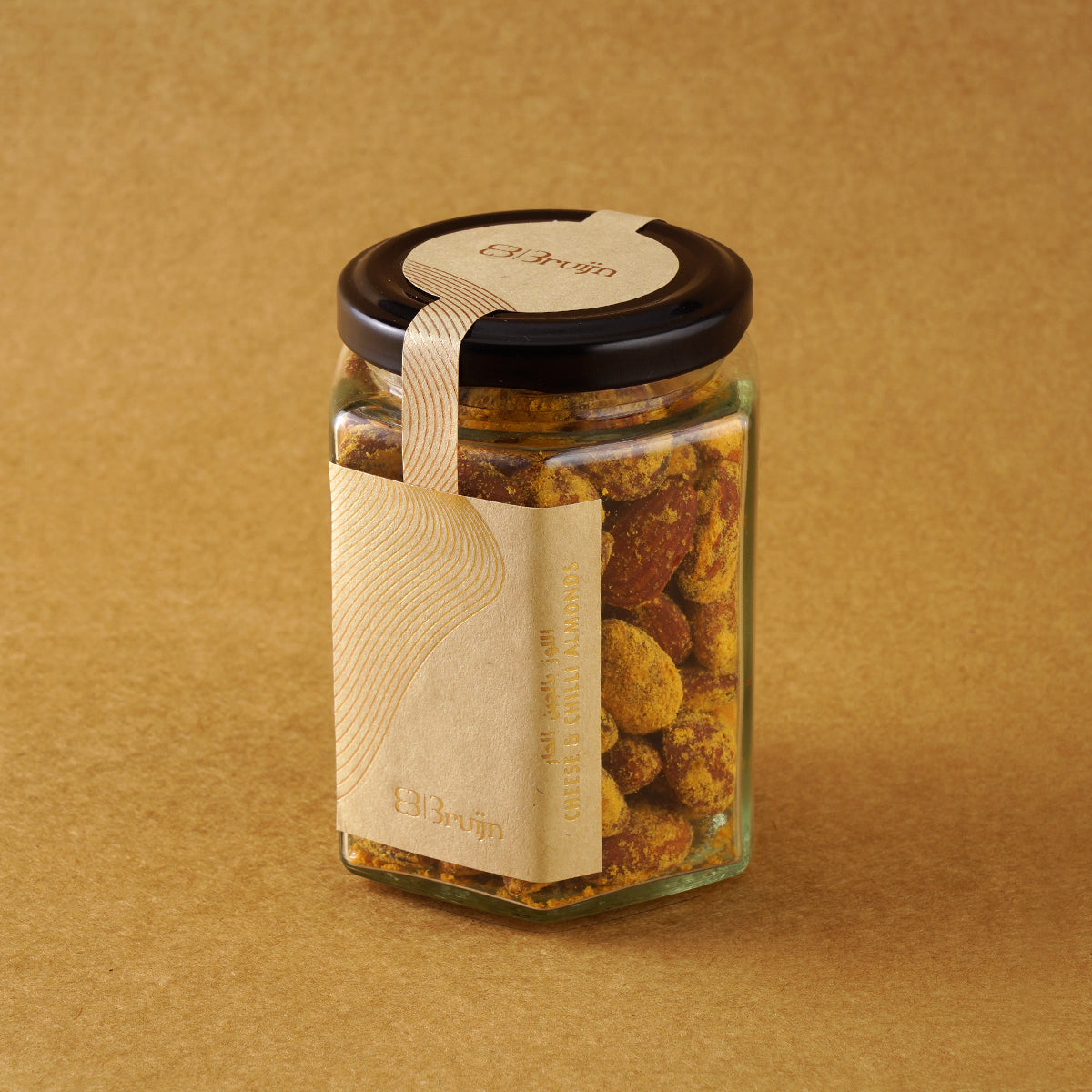 Glass jar of Bruijn Cheese & Chilli Almonds with a black lid and kraft label, showing golden almonds coated in cheese and chilli seasoning.