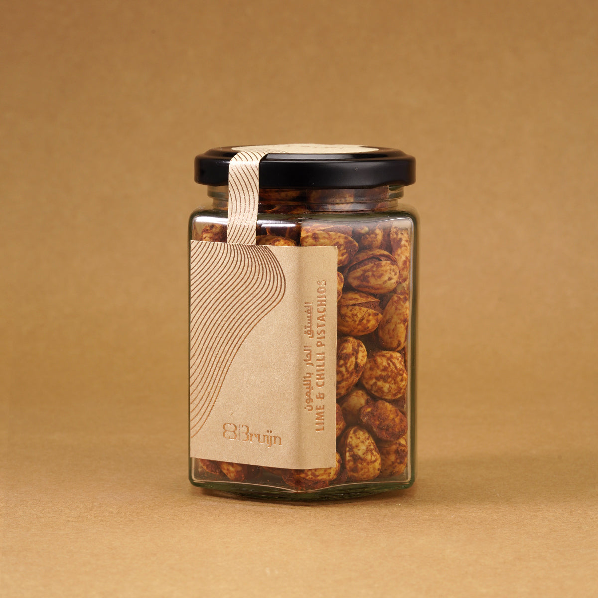 Glass jar of Bruijn Persian Lime & Chilli Pistachios with black lid and kraft label, filled with spiced pistachios coated in lime and chilli seasoning.