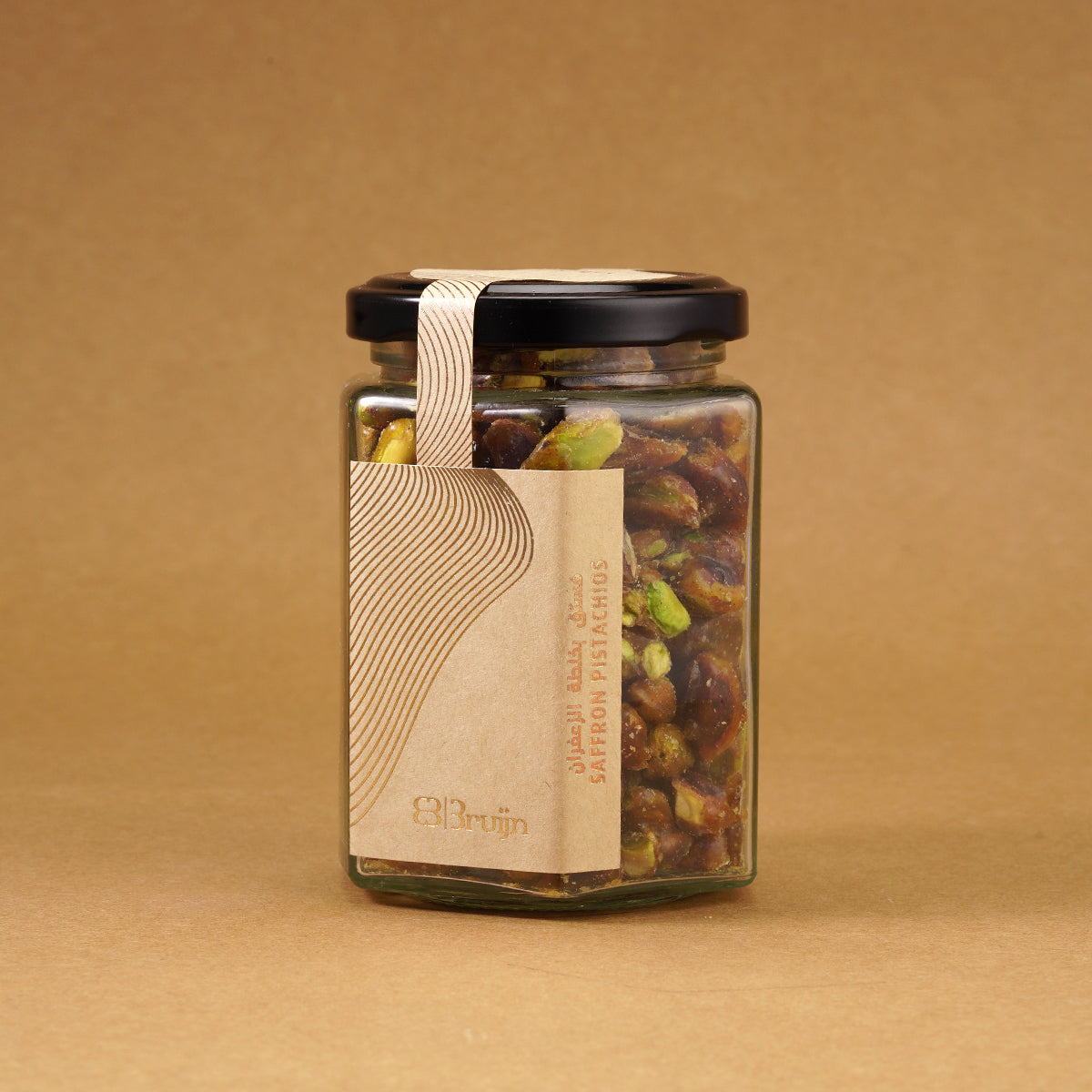 Glass jar of Bruijn Saffron Caramel Pistachios with black lid and kraft label, filled with golden caramel-coated pistachio kernels infused with saffron strands.