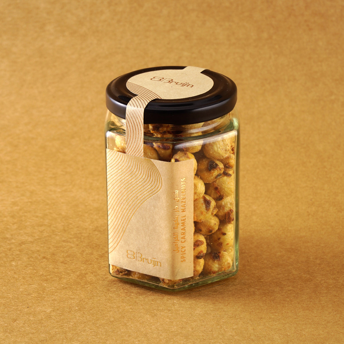 Glass jar of Bruijn Chilli Sweet Hazelnuts with black lid and kraft label, filled with golden hazelnuts coated in cane sugar and speckled with red chilli flakes.