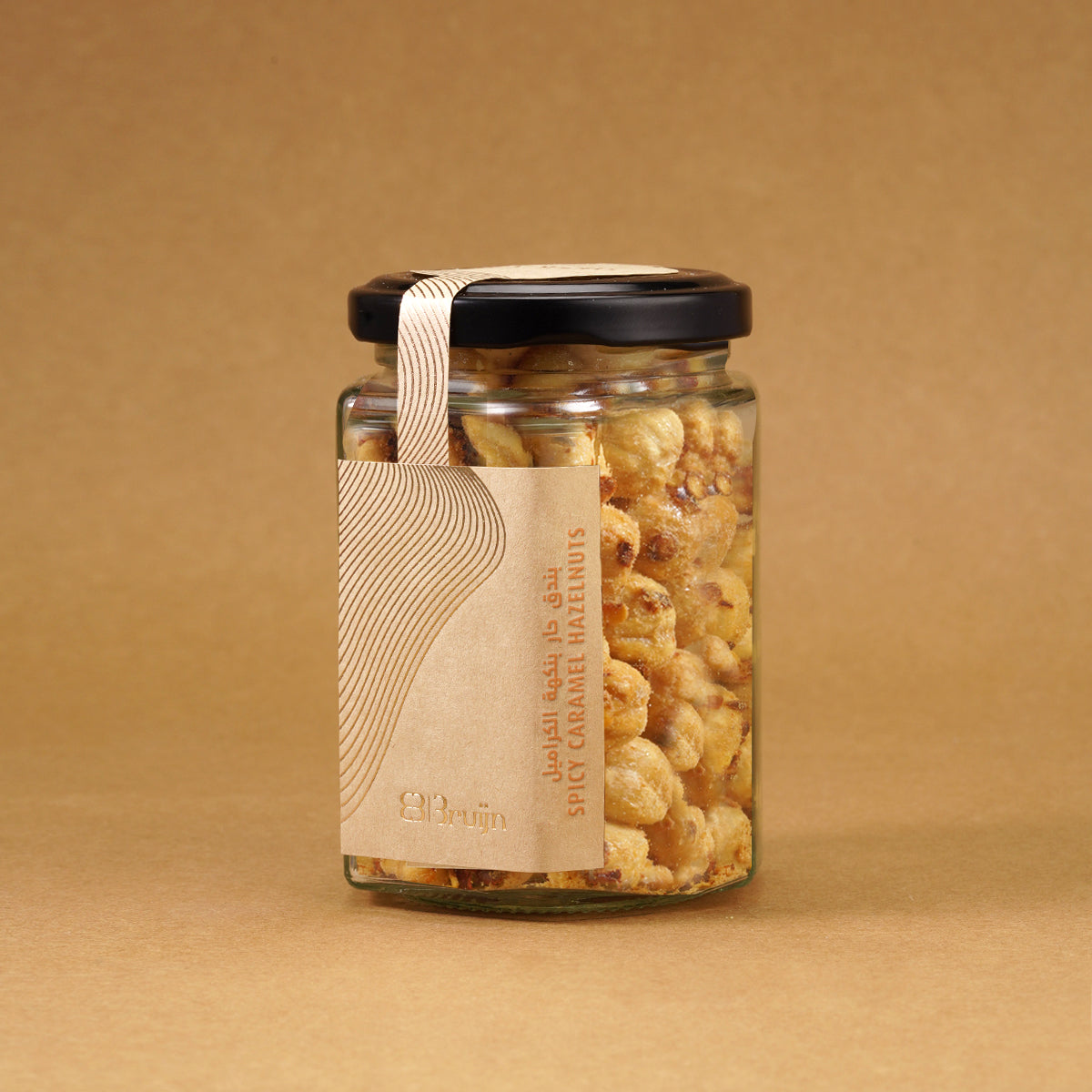 Glass jar of Bruijn Chilli Sweet Hazelnuts with black lid and kraft label, filled with golden hazelnuts coated in cane sugar and speckled with red chilli flakes.