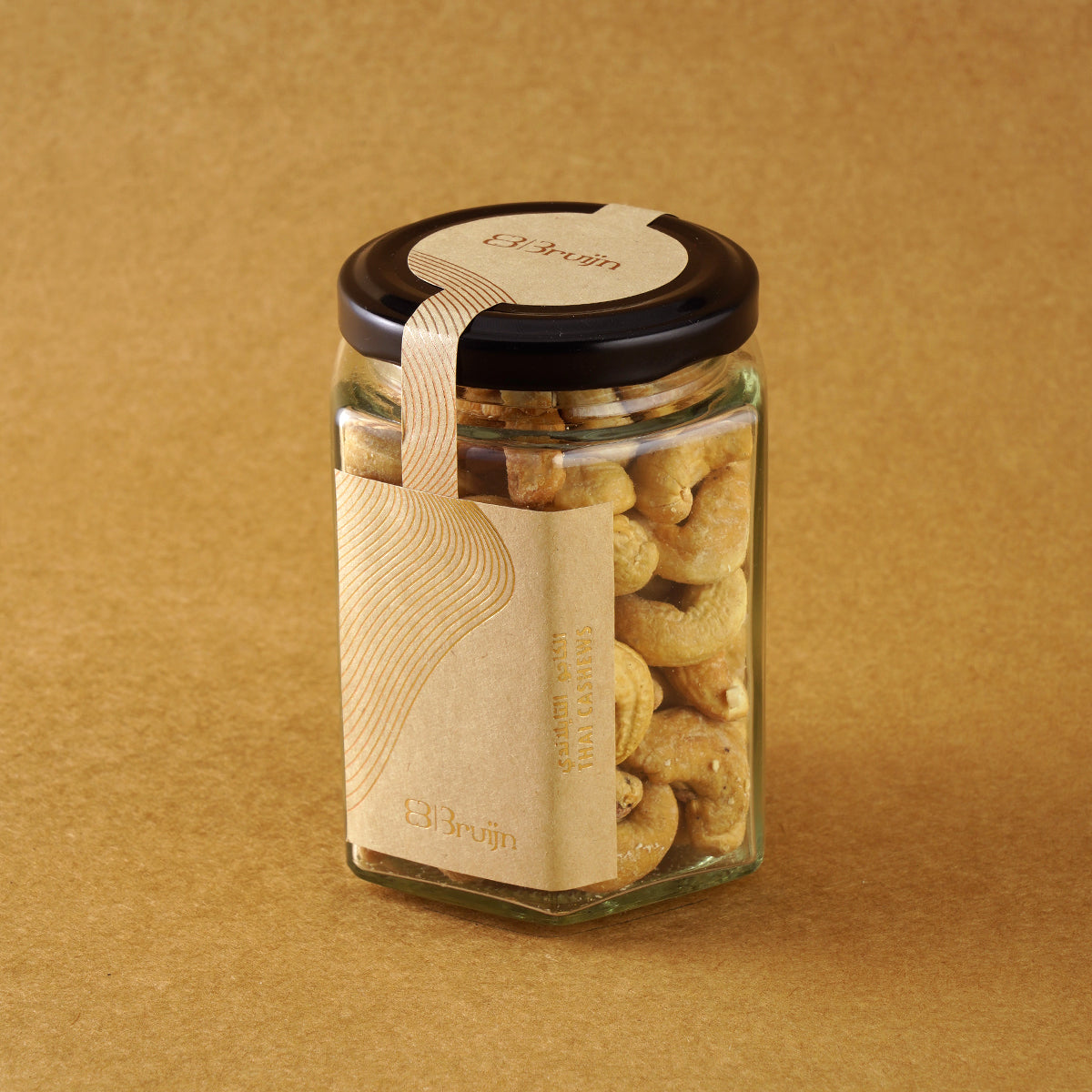 Glass jar of Bruijn Thai Herb Cashews with black lid and kraft label, filled with golden cashews coated in aromatic Thai herbs and spice seasoning.