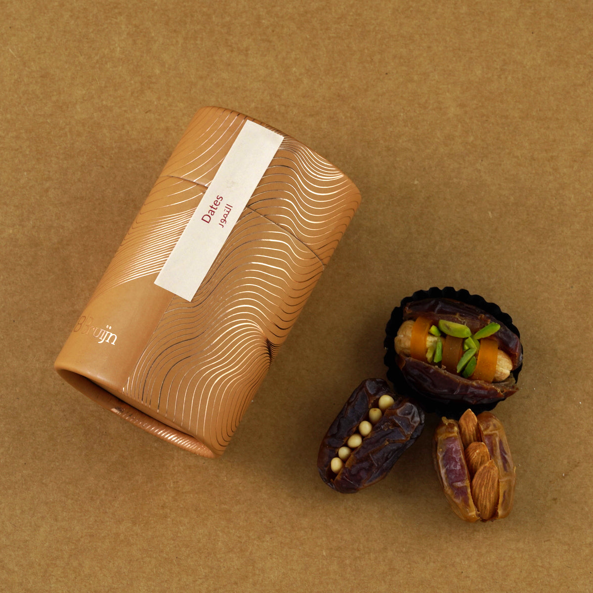 Golden cylindrical container of Bruijn Assorted Stuffed Dates placed beside dates filled with cashew nuts, almonds, mango peel, macadamia nuts, and candied orange peel.