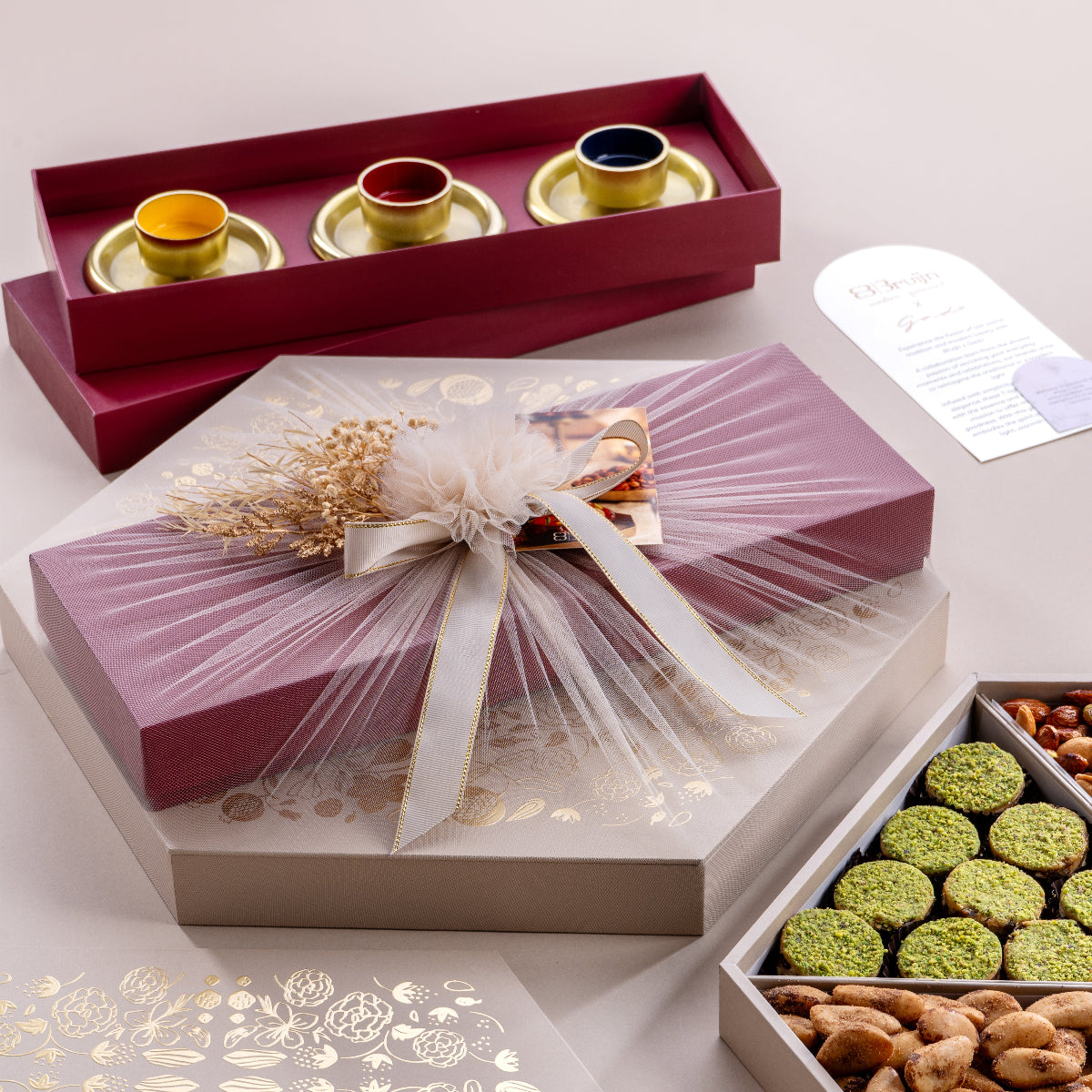 An assortment of freshly made food items including tea light holders, fig and nut bites, salted caramel nut delice, walnut and dried fruit wholes, praline pecan, and smoked Brazilian nuts, presented in a decorative red tray with a white ribbon.