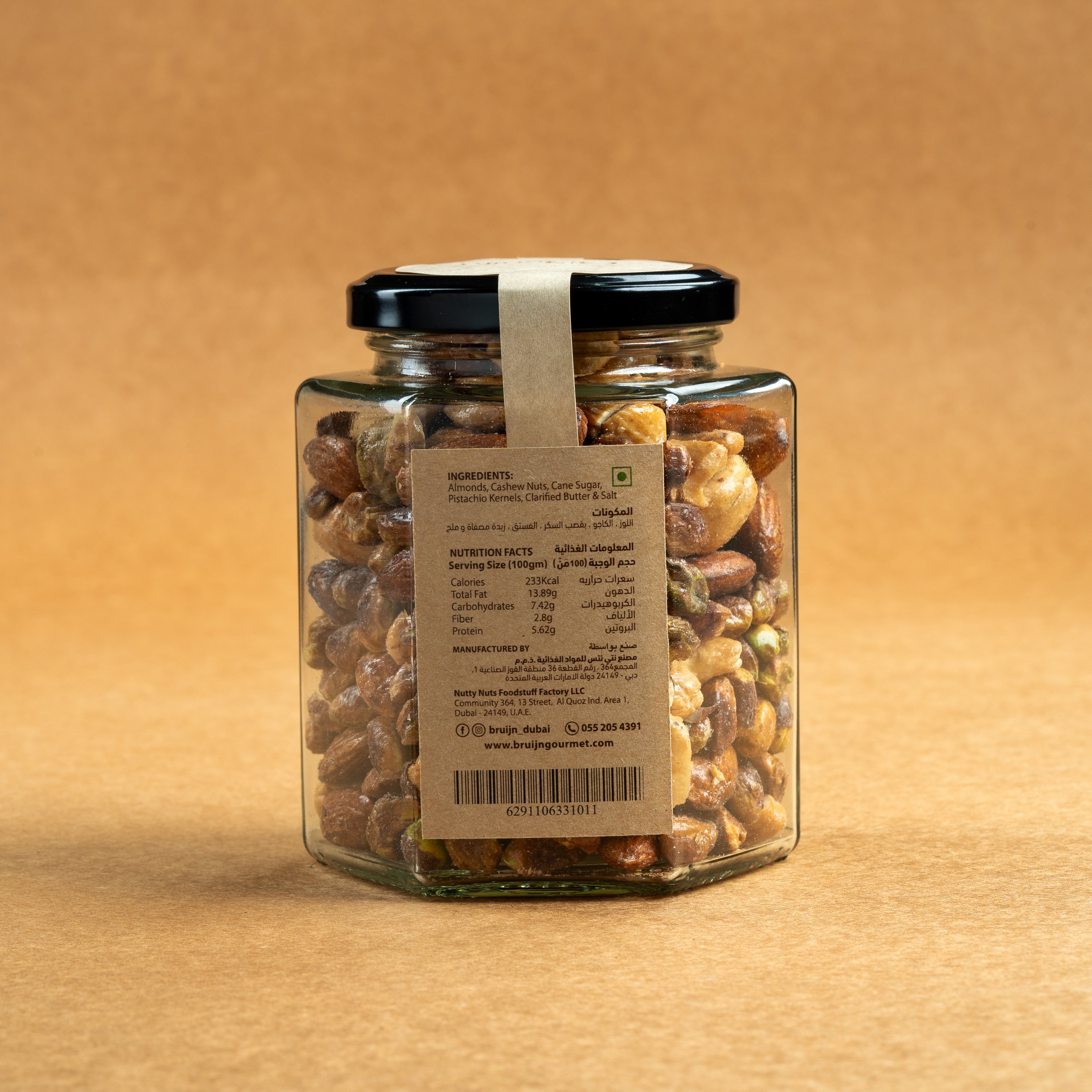 Glass jar of Bruijn Salted Caramel Nut Délice with black lid and elegant kraft label, filled with cashews, almonds, and pistachios coated in golden caramel.
