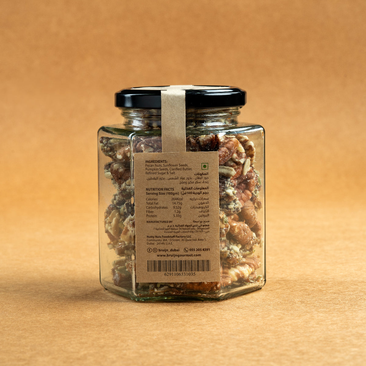 Glass jar of Bruijn Praline Pecans with black lid and kraft label, filled with caramel-coated pecans encrusted with roasted seeds for a sweet and crunchy treat.