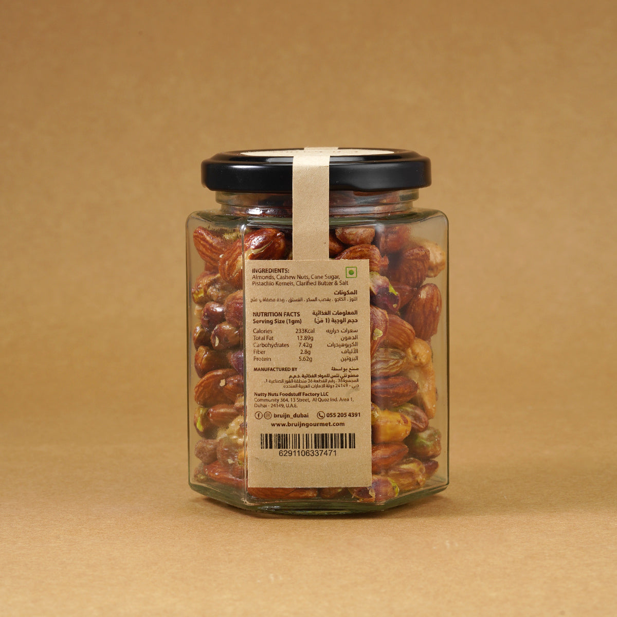 Glass jar of Bruijn Salted Caramel Nut Délice with black lid and elegant kraft label, filled with cashews, almonds, and pistachios coated in golden caramel.