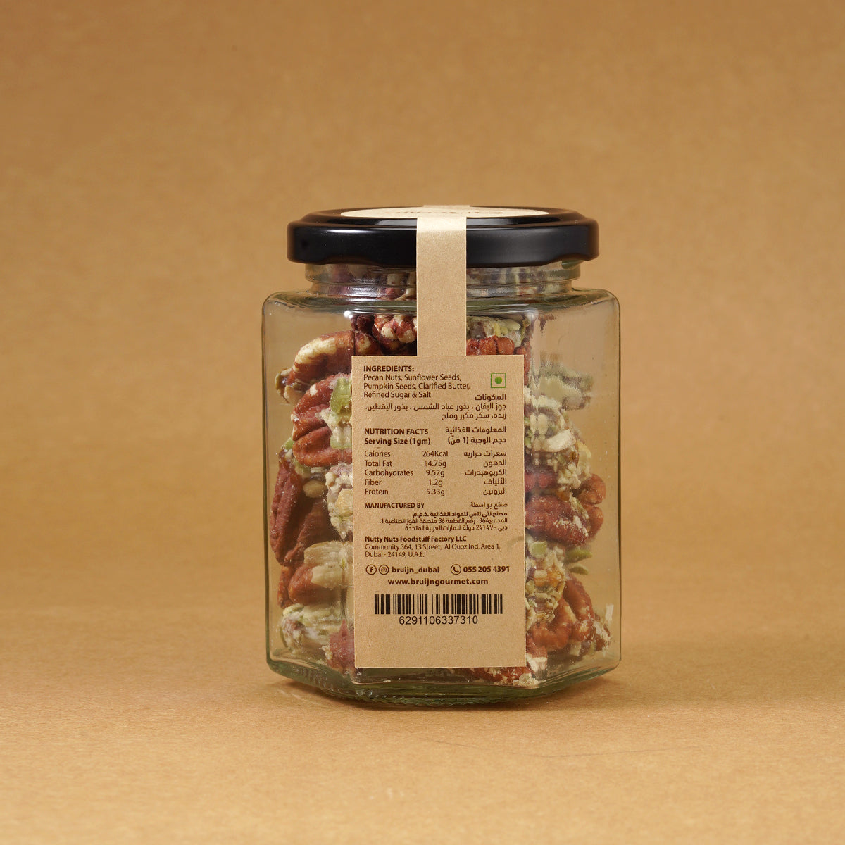 Glass jar of Bruijn Praline Pecans with black lid and kraft label, filled with caramel-coated pecans encrusted with roasted seeds for a sweet and crunchy treat.