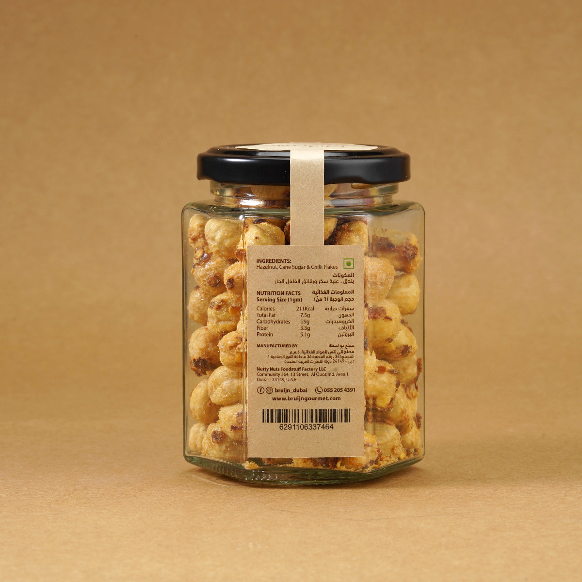 Glass jar of Bruijn Chilli Sweet Hazelnuts with black lid and kraft label, filled with golden hazelnuts coated in cane sugar and speckled with red chilli flakes.